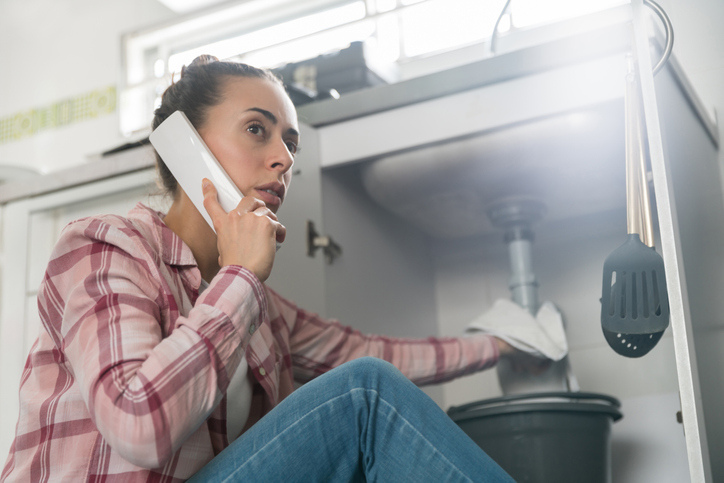 Woman at home calling a plumber about a leaking pipe in her sink